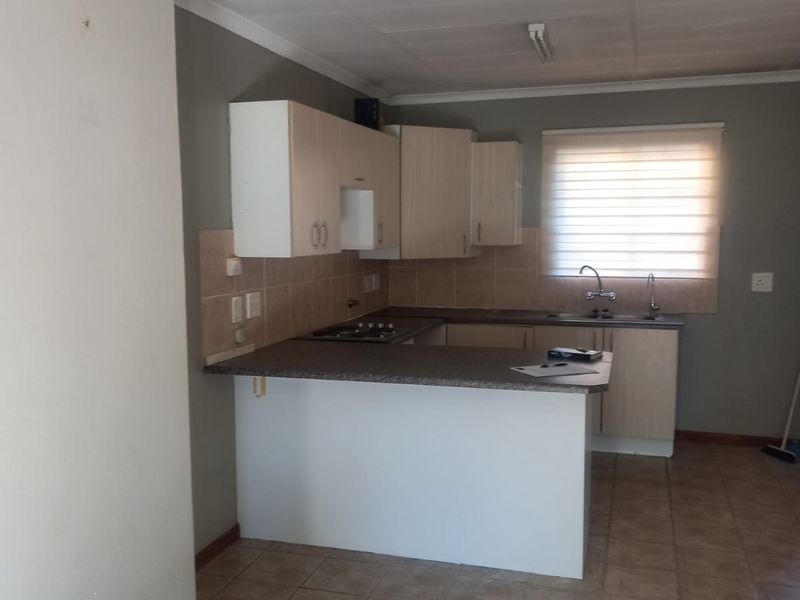 A functional kitchen featuring laminate cabinetry, built-in hob, stainless steel sink, and tiled flooring, offering a practical layout ready for modern updates.
