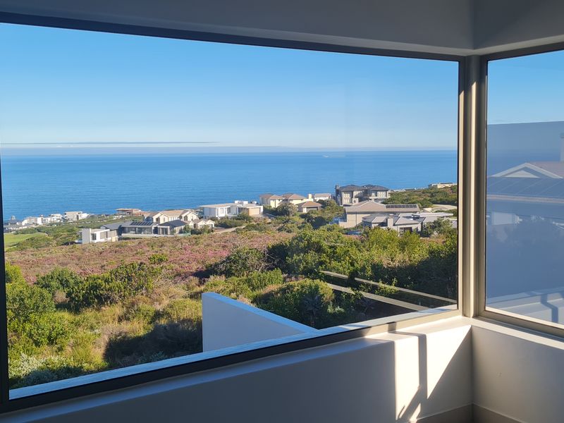 A stunning elevated view of the coastline and surrounding residential estate, captured through large, modern aluminium-framed windows.