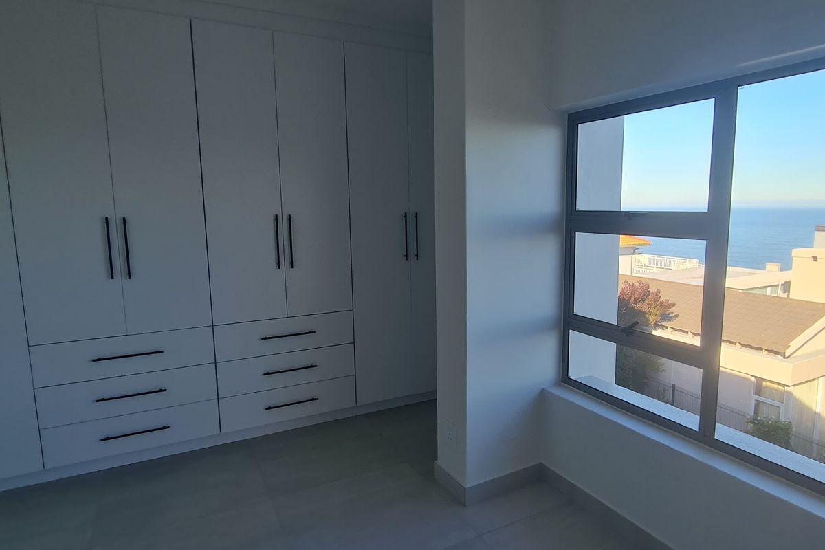 A bright, modern bedroom featuring extensive built-in cabinetry, tiled flooring, and large windows offering scenic coastal views.