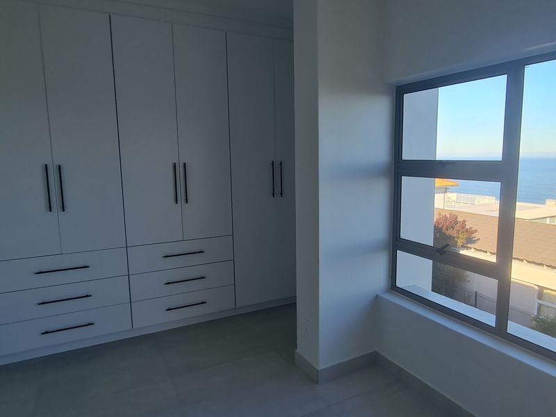 A bright, modern bedroom featuring extensive built-in cabinetry, tiled flooring, and large windows offering scenic coastal views.