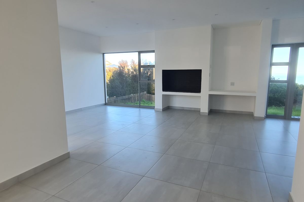 Spacious, modern open-plan living area featuring large windows, neutral tiled flooring, and a built-in fireplace, offering a bright and clean aesthetic.