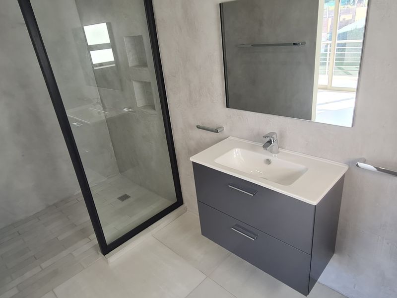 Modern bathroom featuring a walk-in shower with black frame, concrete-look wall finishes, and a contemporary vanity unit with integrated basin.