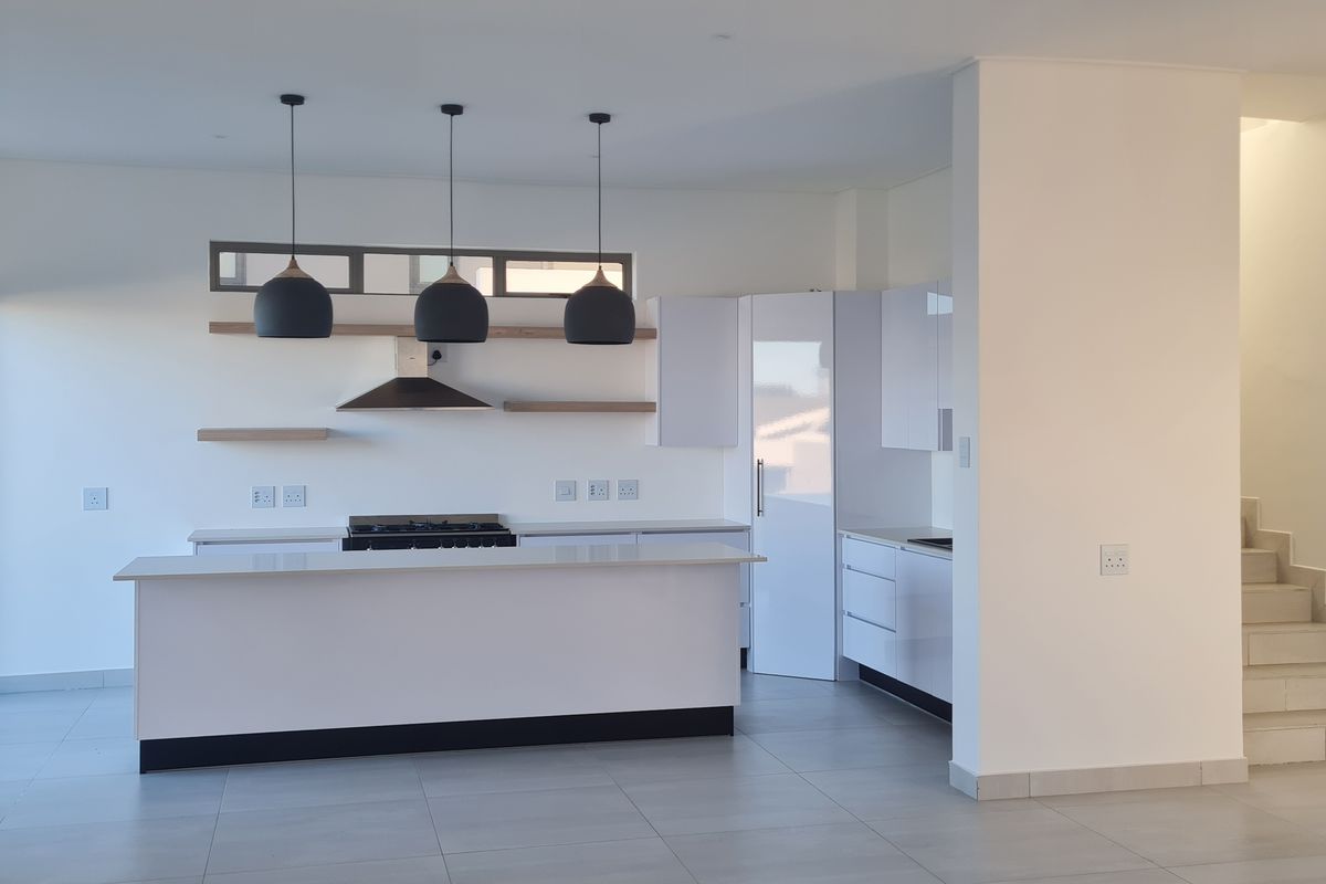Modern open-plan kitchen featuring a central island, gas hob, sleek white cabinetry, and contemporary pendant lighting, seamlessly connected to the living area and staircase.
