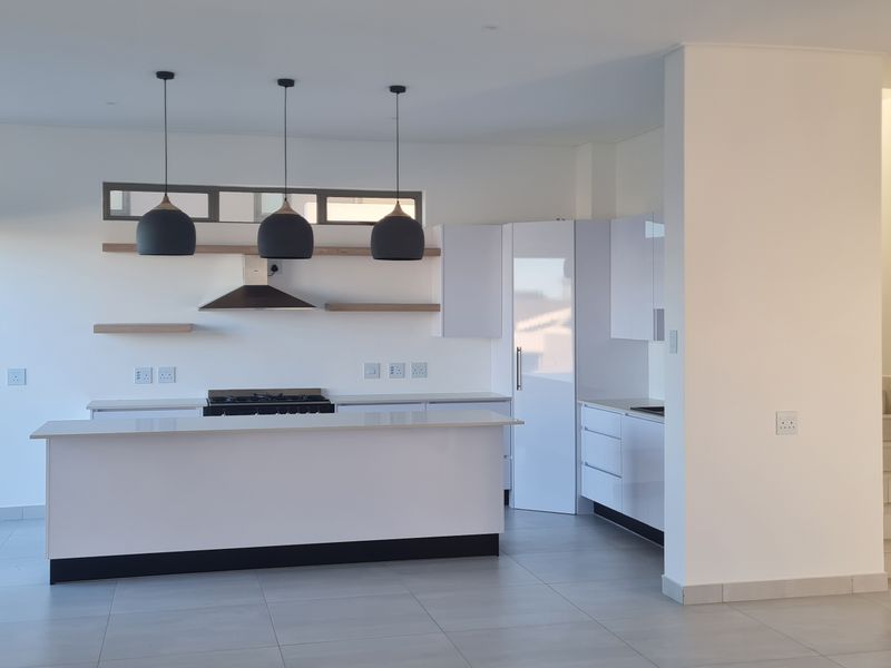 Modern open-plan kitchen featuring a central island, gas hob, sleek white cabinetry, and contemporary pendant lighting, seamlessly connected to the living area and staircase.
