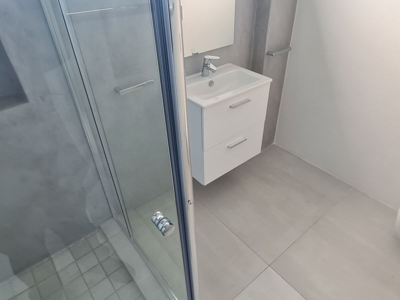 Modern bathroom featuring a wall-mounted vanity, glass shower enclosure with a recessed niche, and a wall-mounted toilet with neutral large format tiling.