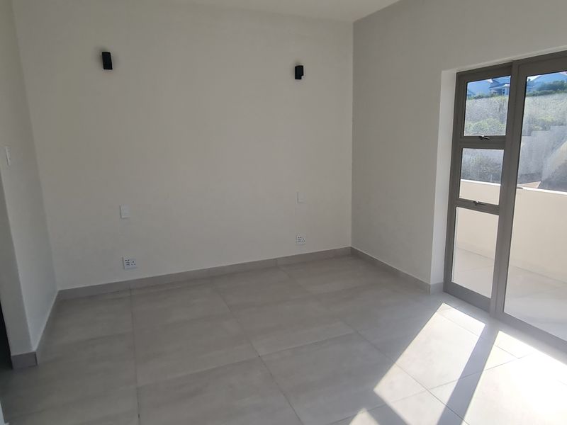 A bright, empty bedroom featuring modern tiled flooring and large aluminium sliding doors providing access to an outdoor area.