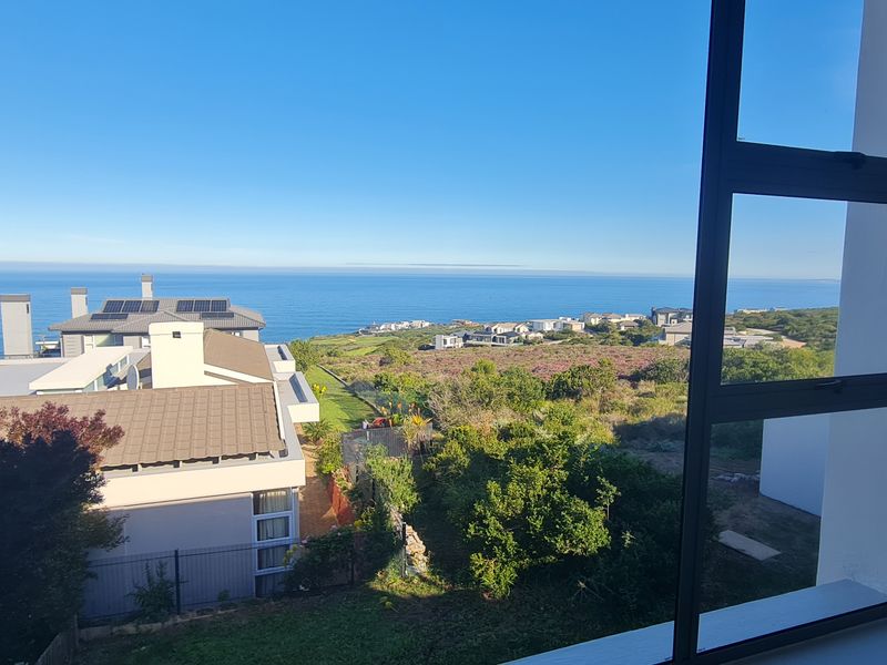 A clear, elevated view of the coastline and surrounding residential area captured through a modern aluminium-framed window.