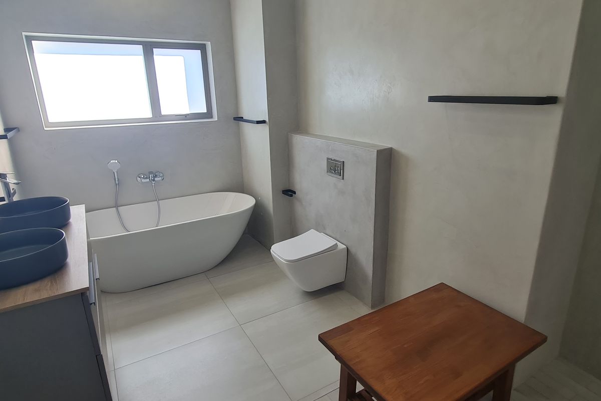 Modern bathroom featuring a sleek freestanding bathtub, wall-mounted toilet, double vessel sink vanity, and contemporary plastered wall finishes.