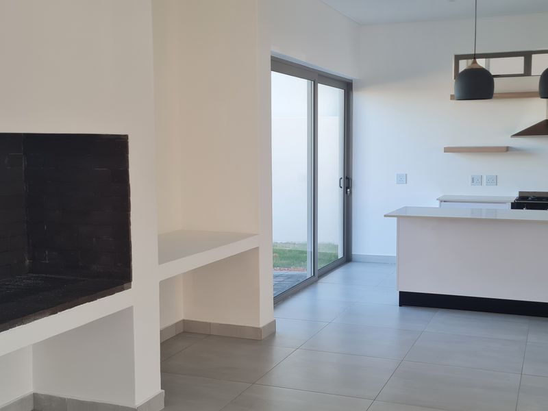 Modern open-plan living area featuring a built-in fireplace, sleek kitchen with island, gas hob, extractor fan, and direct access to the outdoor space.