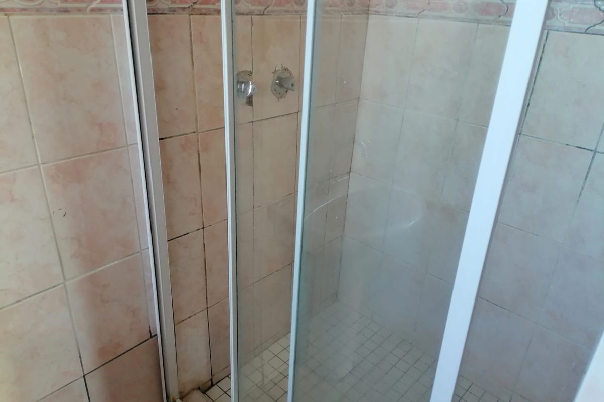 A dated bathroom shower enclosure featuring tiled walls and flooring, currently requiring maintenance and fixture replacement.