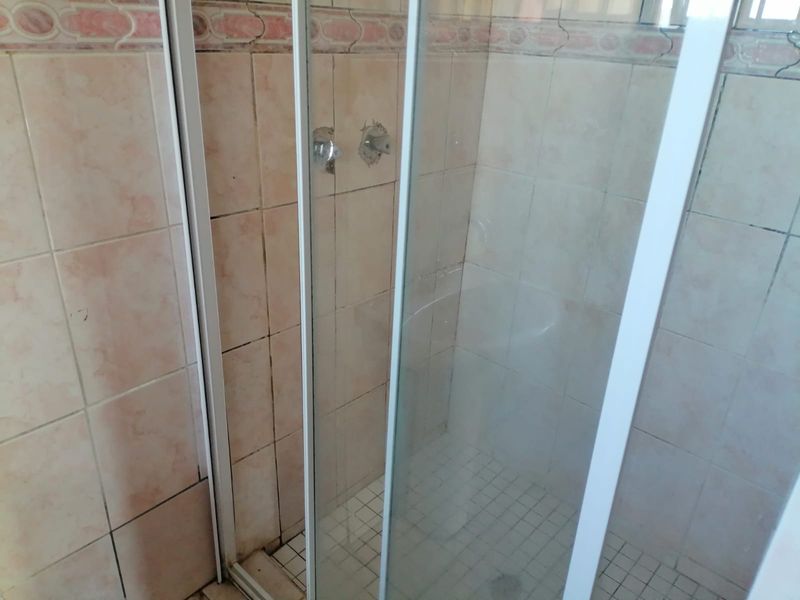 A dated bathroom shower enclosure featuring tiled walls and flooring, currently requiring maintenance and fixture replacement.
