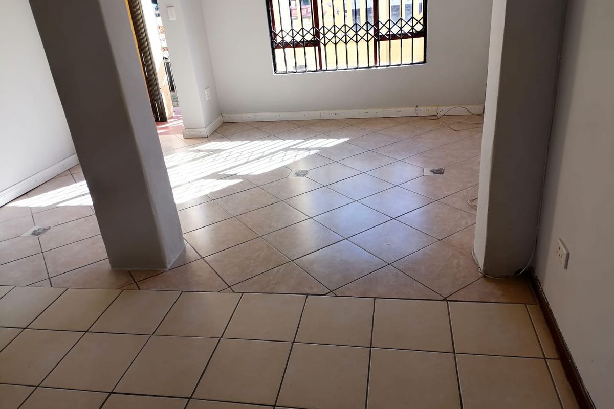 An empty, open-plan living area featuring neutral tiled flooring, structural columns, and windows fitted with security bars.