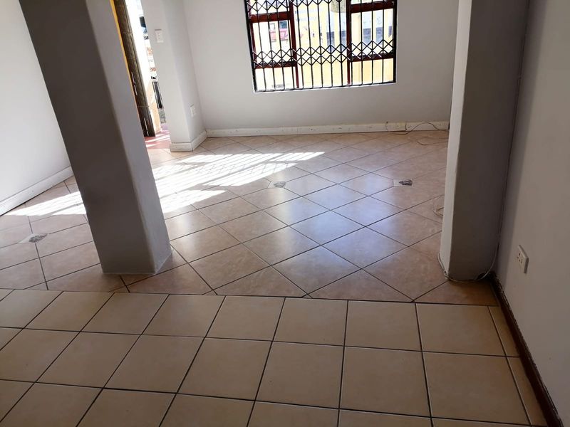 An empty, open-plan living area featuring neutral tiled flooring, structural columns, and windows fitted with security bars.