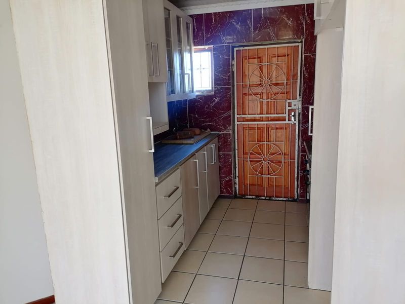 A compact kitchen featuring built-in cabinetry, laminate countertops, tiled flooring, and a secure exterior door with a metal security gate.
