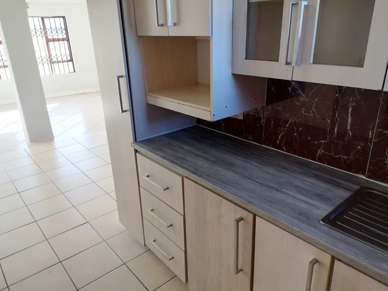 A functional kitchen area featuring laminate cabinetry, a dark marble-effect backsplash, and tiled flooring, with an open-plan layout leading to an adjacent living space.