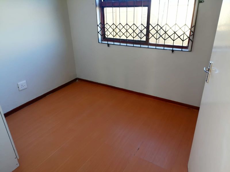 A vacant bedroom featuring laminate flooring, neutral walls, and a window fitted with a security gate.
