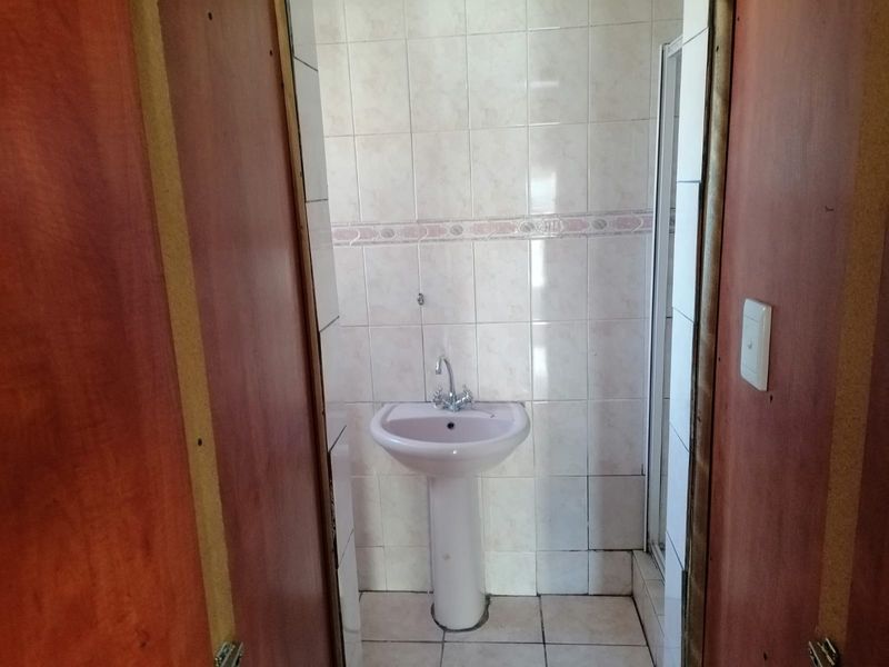 A compact bathroom featuring a pedestal basin, tiled walls, and a shower enclosure, requiring cosmetic updates to modernize the space.
