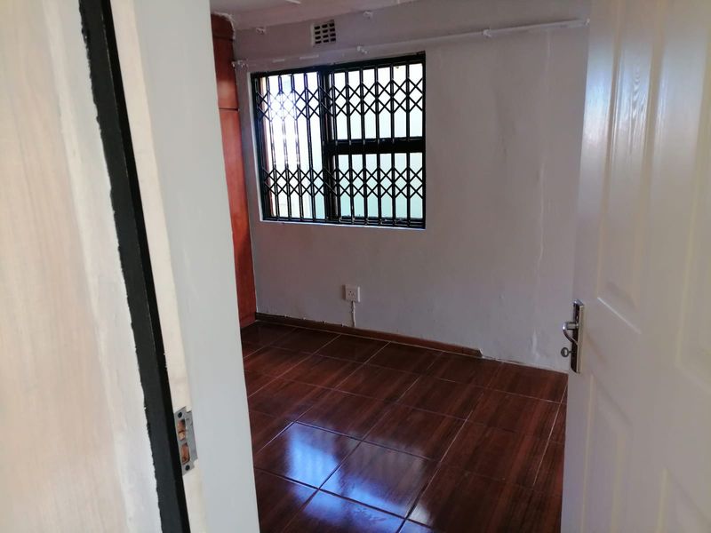 An empty bedroom featuring dark wood-look tiled flooring, a built-in cupboard, and a window fitted with a security gate.