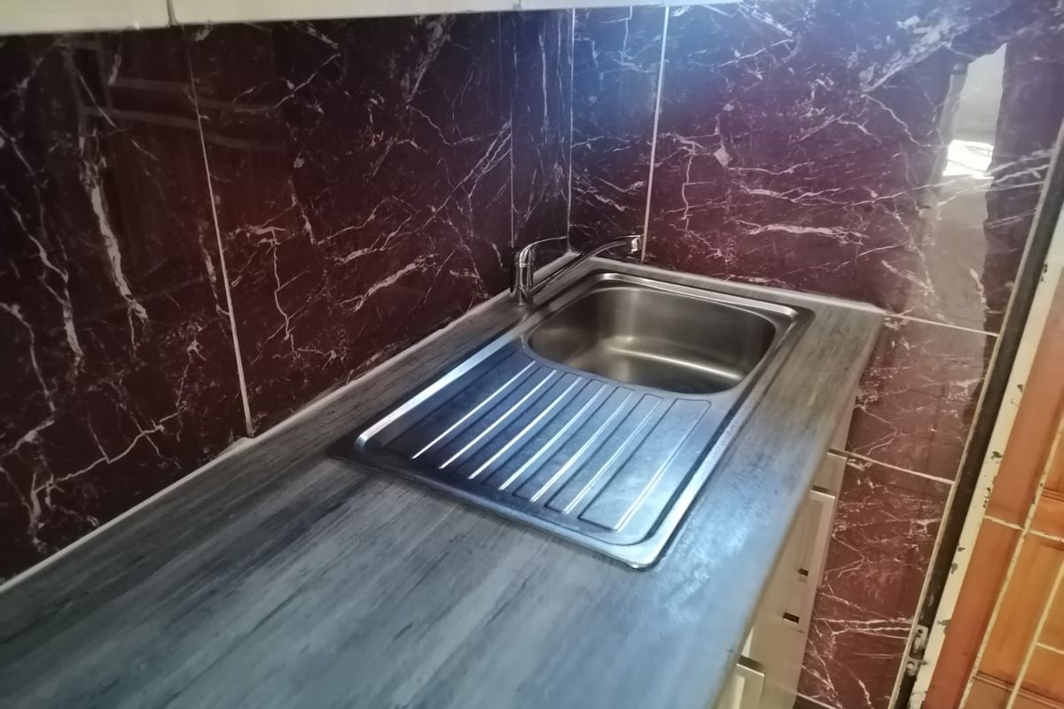 A compact kitchen area featuring a stainless steel sink, laminate countertop, and distinctive dark marble-effect wall tiling.