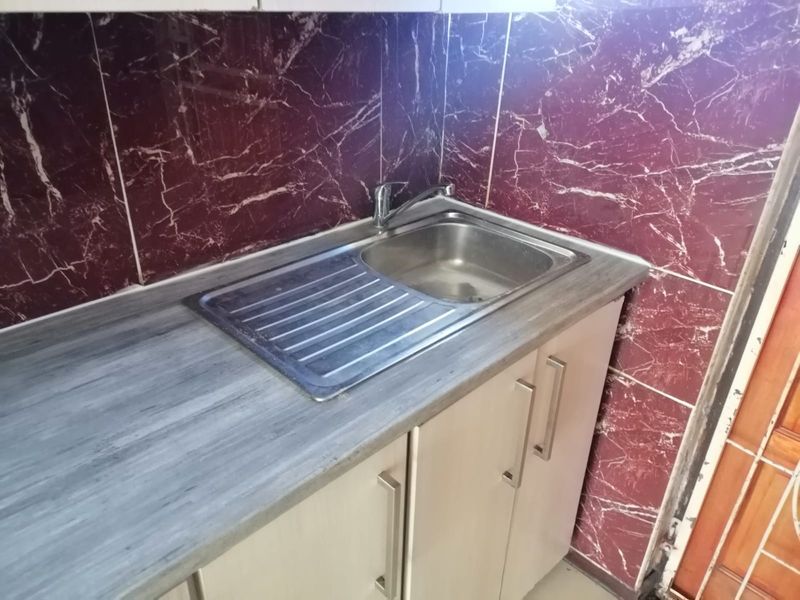 A compact kitchen area featuring a stainless steel sink, laminate countertop, and distinctive dark marble-effect tiled splashback with base cabinetry.