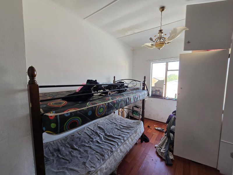 A bedroom featuring timber flooring, a built-in cupboard, and a ceiling light fixture, currently showing signs of wear and ceiling water damage.