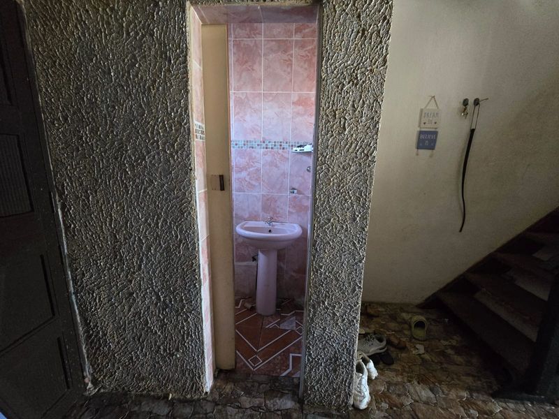 A small bathroom featuring a pedestal sink with pink wall tiling and textured wall finishes, requiring significant cosmetic updates and repairs.