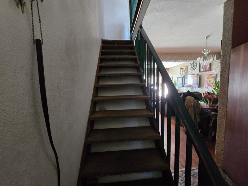 A staircase with a metal balustrade leading to an upper level, showing signs of wear on the carpeted treads and painted finishes.