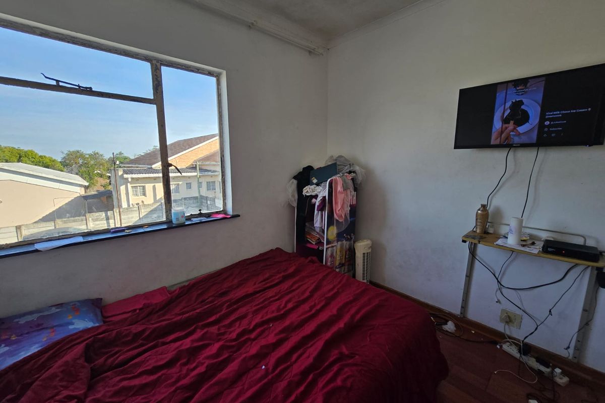 A bedroom featuring laminate flooring and a steel-framed window with exterior views. The room requires cosmetic updates to the walls and ceiling.