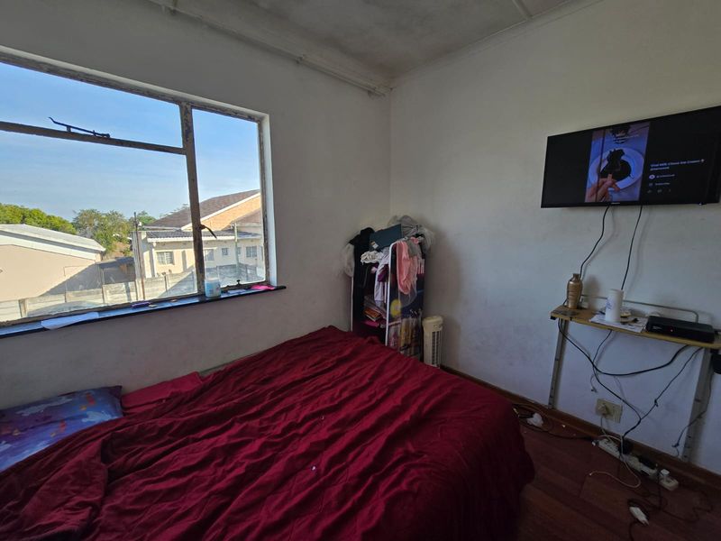 A bedroom featuring laminate flooring and a steel-framed window with exterior views. The room requires cosmetic updates to the walls and ceiling.