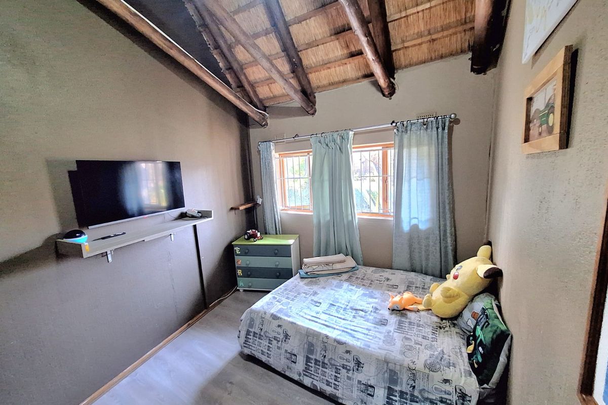 A bedroom featuring a rustic thatched roof with exposed timber rafters, laminate flooring, and security bars on the windows.