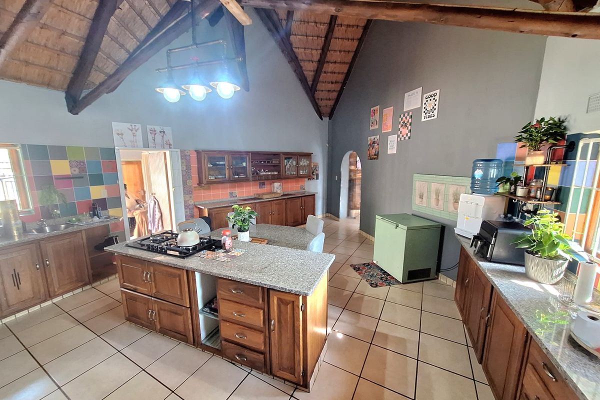 Spacious kitchen featuring a central island with granite countertops, wooden cabinetry, gas hob, and high vaulted ceilings with exposed timber trusses.