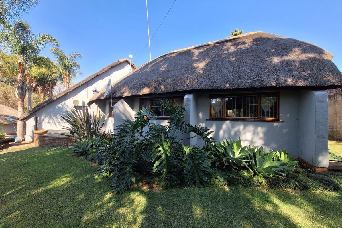 Rear view of a house featuring a traditional thatched roof, timber-framed windows with security bars, and a landscaped garden area.