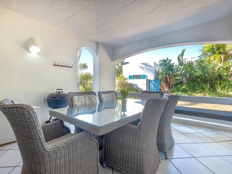 A covered patio area featuring tiled flooring, a built-in bench, and an arched opening leading to a private garden space.