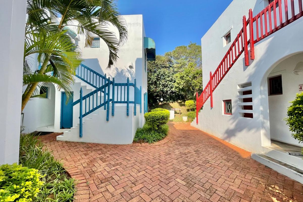 A well-maintained exterior courtyard featuring brick paving, landscaped garden beds, and external staircases providing access to upper-level apartment units.