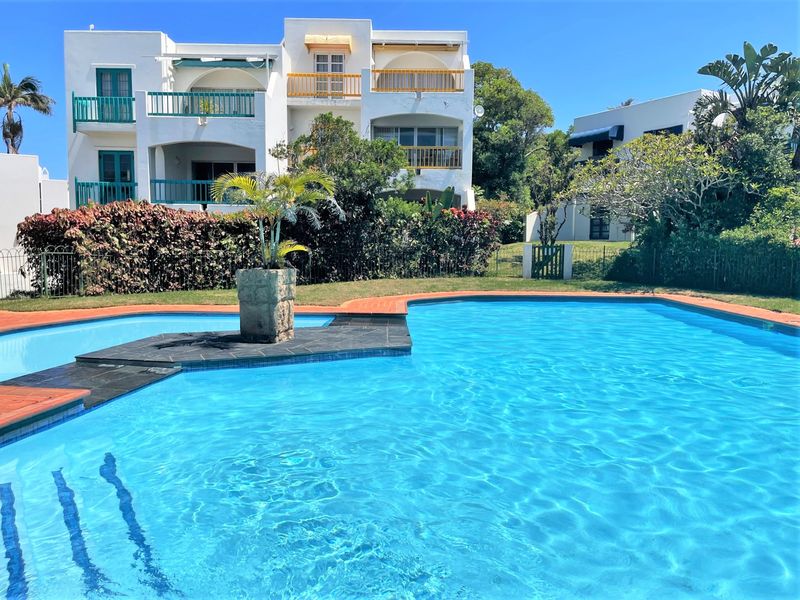A well-maintained communal swimming pool area featuring paved surrounds, landscaped gardens, and views of the apartment building's balconies.