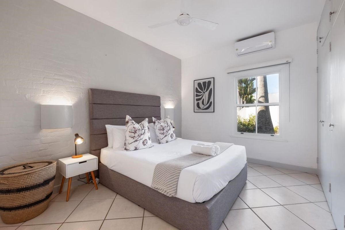 A well-maintained bedroom featuring tiled flooring, a painted brick feature wall, ceiling fan, and a split-system air conditioner.