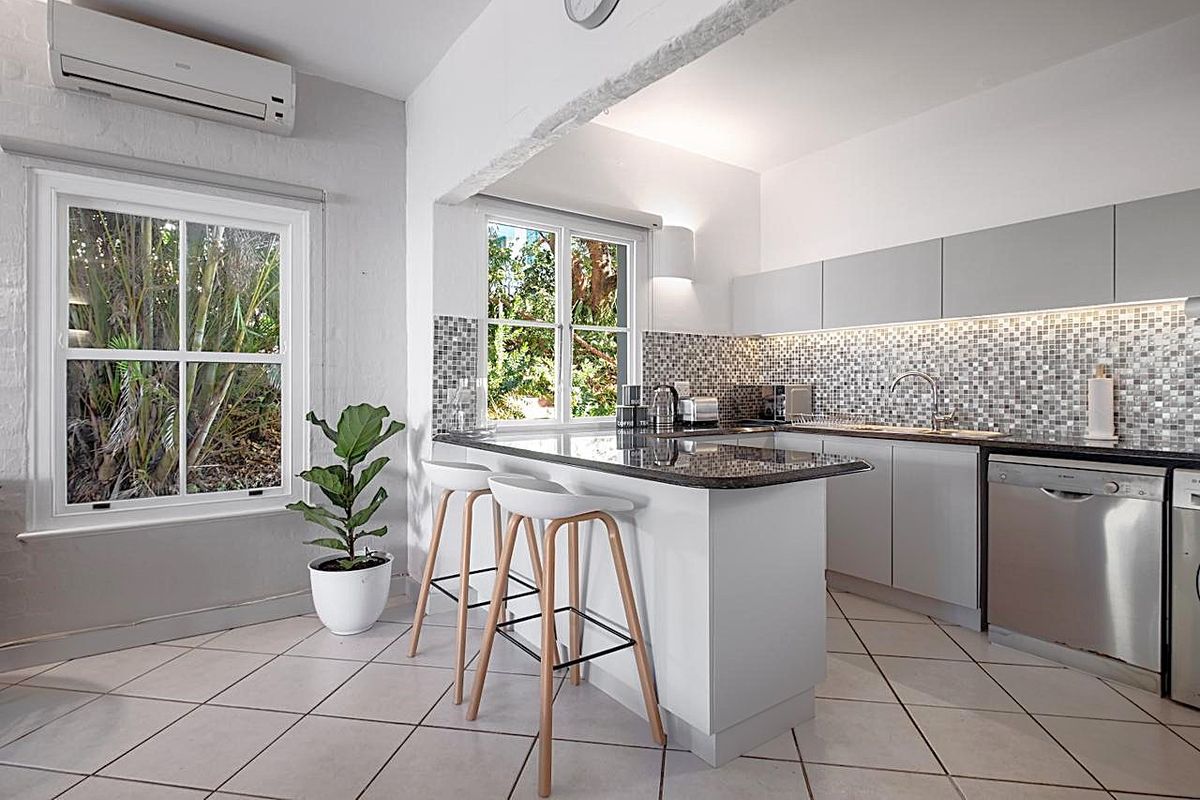 Modern kitchen featuring granite countertops, mosaic tile backsplash, integrated dishwasher, and a split-system air conditioner, offering a clean and functional workspace.