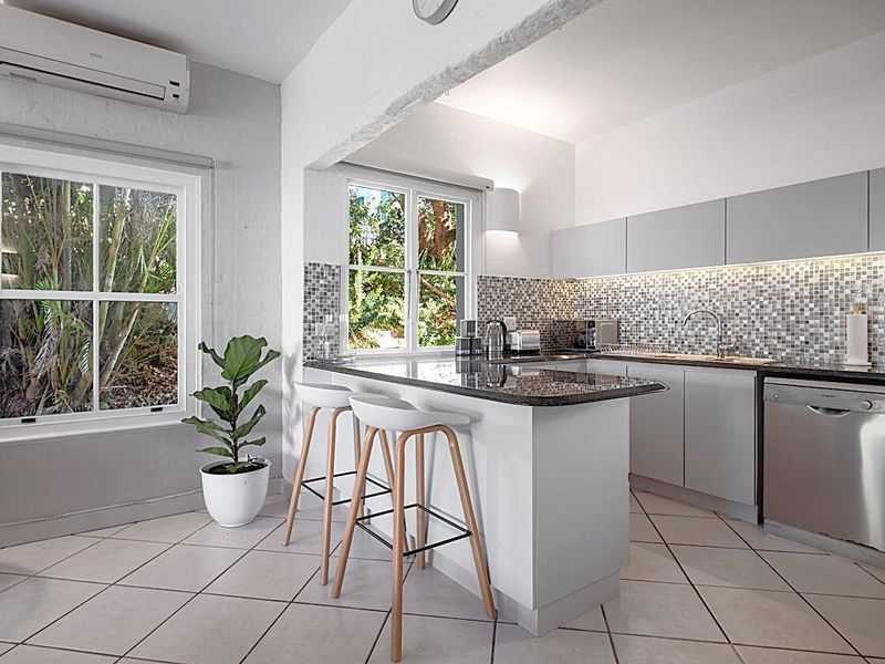 Modern kitchen featuring granite countertops, mosaic tile backsplash, integrated dishwasher, and a split-system air conditioner, offering a clean and functional workspace.