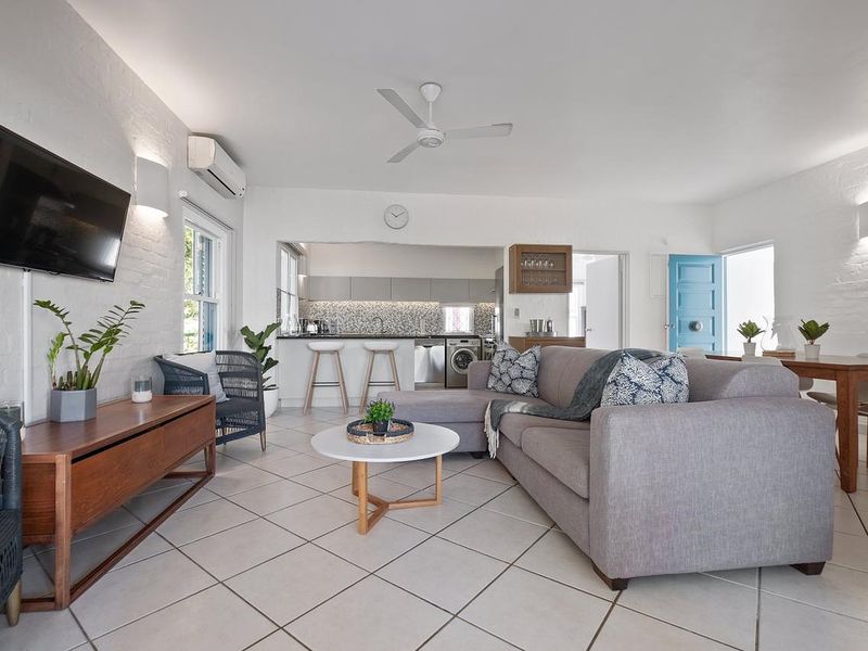 Bright open-plan living and dining area featuring tiled floors, exposed brick walls, and a modern kitchen with integrated appliances and a breakfast bar.