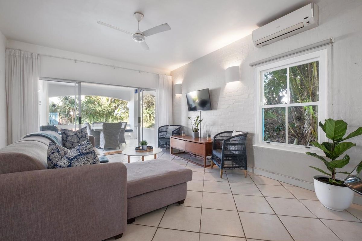 Bright living room featuring painted brick walls, ceramic tile flooring, a ceiling fan, split-system air conditioning, and large sliding doors leading to a patio.