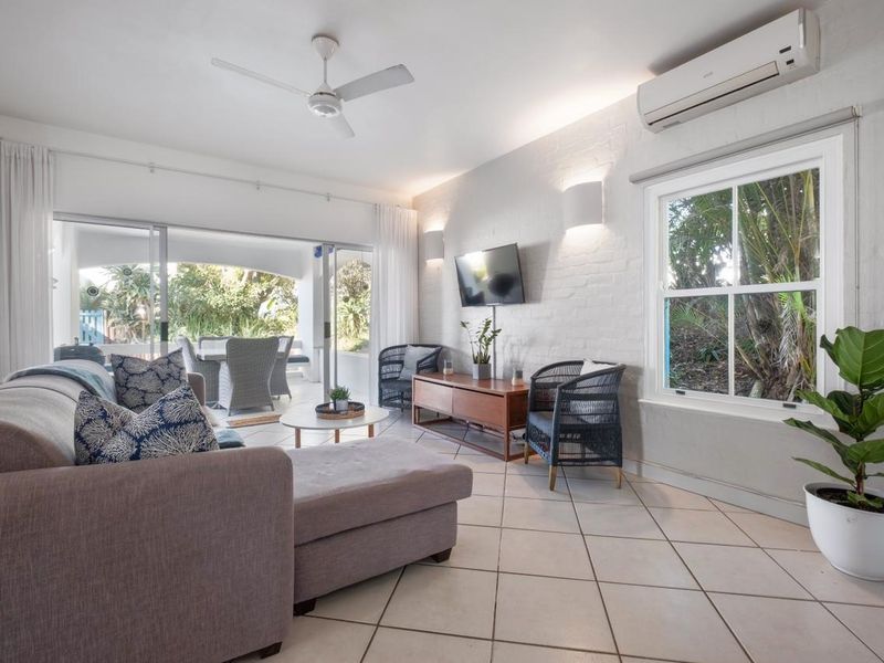 Bright living room featuring painted brick walls, ceramic tile flooring, a ceiling fan, split-system air conditioning, and large sliding doors leading to a patio.