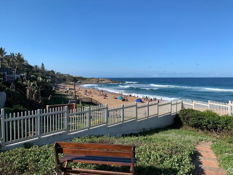 A scenic coastal view overlooking the beach, featuring a secure perimeter fence and landscaped grounds.