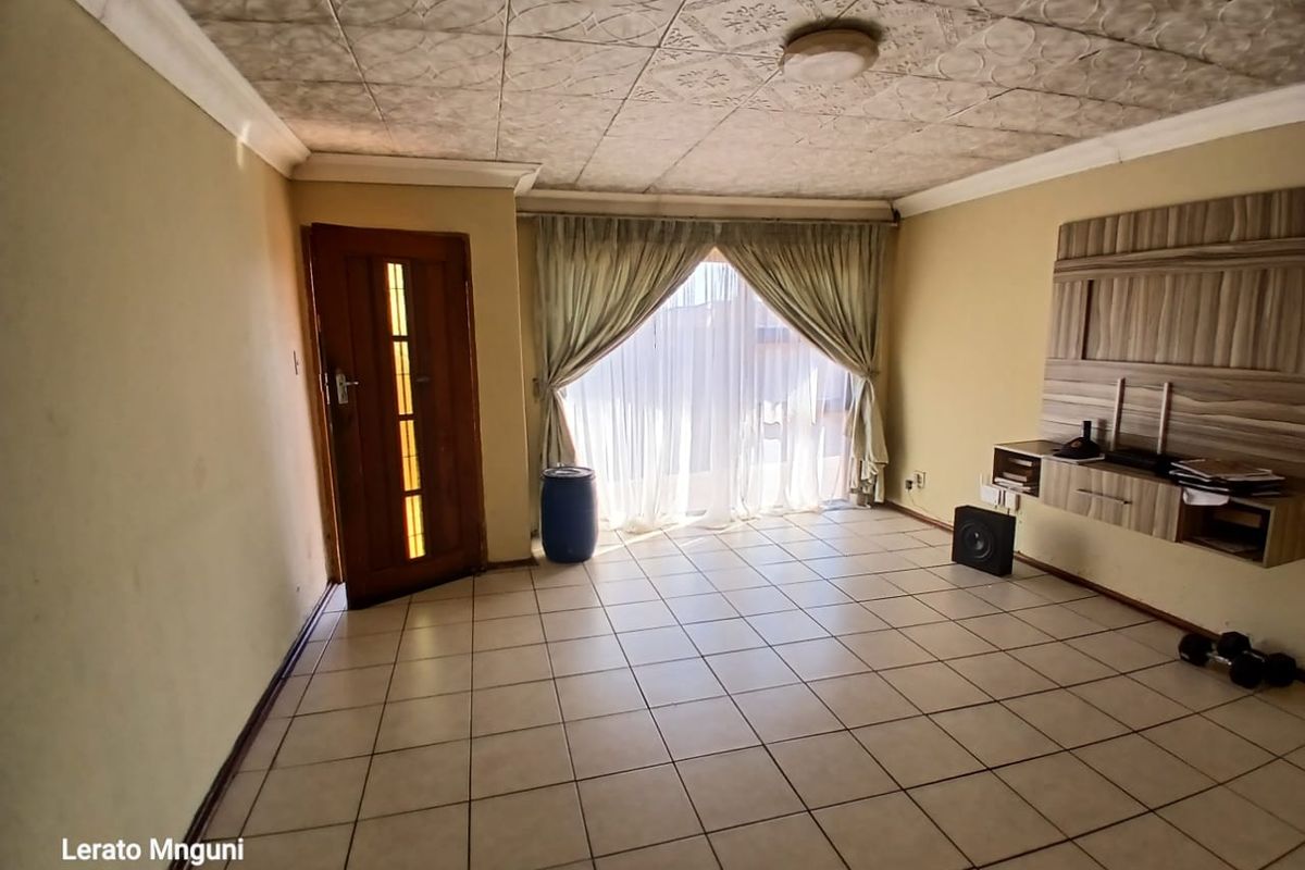 A spacious living room featuring tiled flooring, a textured ceiling, and a built-in media console, offering a blank canvas for interior design updates.
