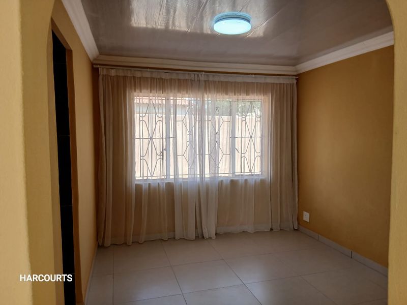 A clean, empty bedroom featuring tiled flooring, security bars on the windows, and a simple ceiling light fixture.