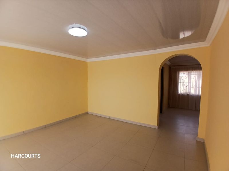 A spacious, empty living room featuring neutral yellow walls, tiled flooring, and an arched entryway leading to an adjacent room.