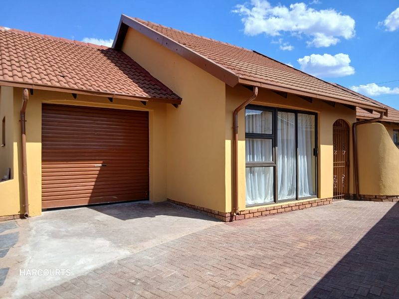 Front exterior view of the house featuring a tiled roof, roller garage door, paved driveway, and aluminium window frames.