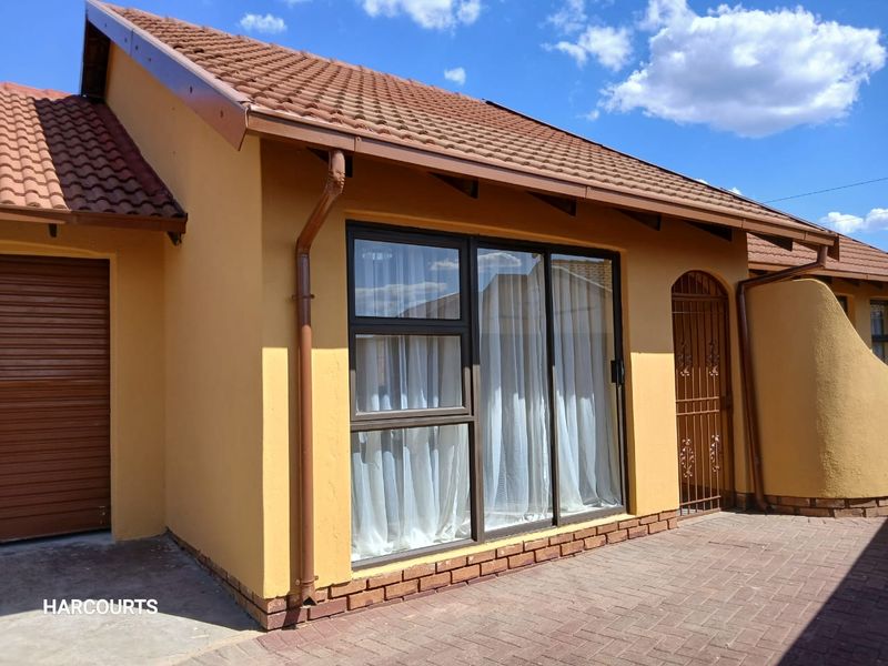 A well-maintained rear exterior view featuring a tiled roof, plastered walls, brick paving, and a secure sliding glass door entrance.