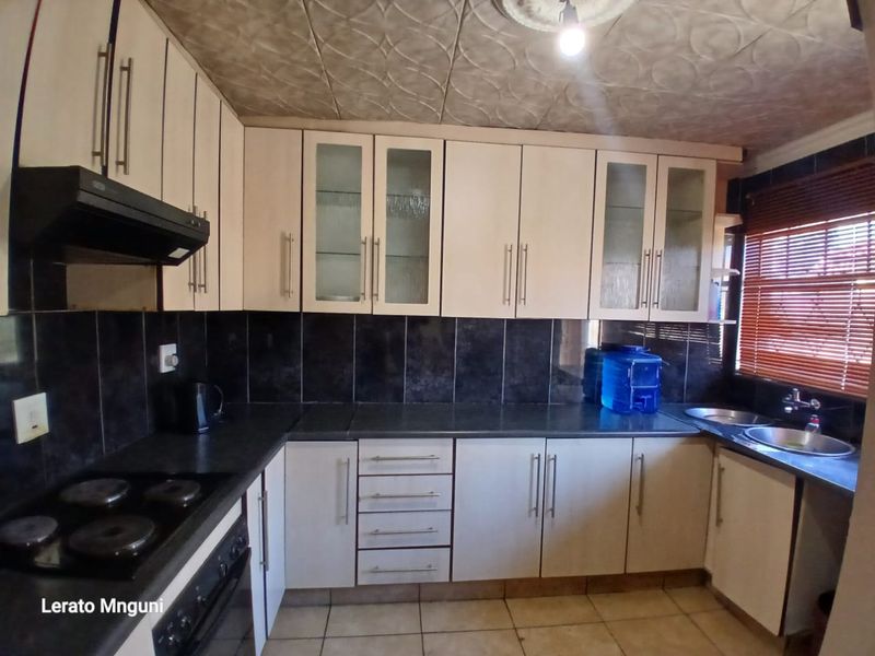 A functional kitchen featuring built-in cabinetry, an electric hob with extractor, and a double sink, finished with tiled backsplash and flooring.