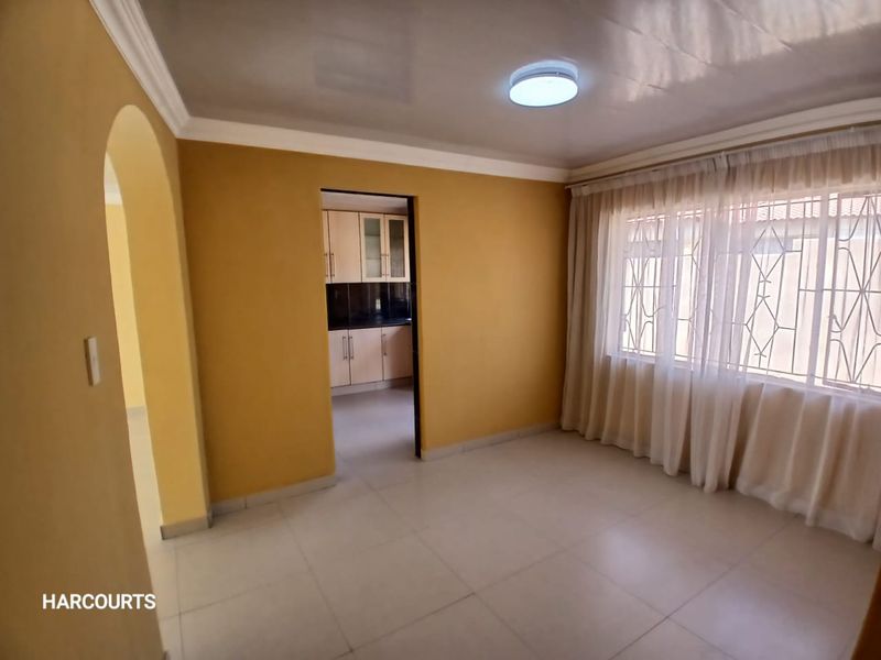 A bright, empty living room featuring tiled flooring, an arched entryway, and a view into the adjacent kitchen area.