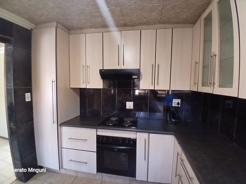 Compact kitchen featuring built-in cabinetry, black tiled backsplash, integrated oven, and electric hob with overhead extractor fan.